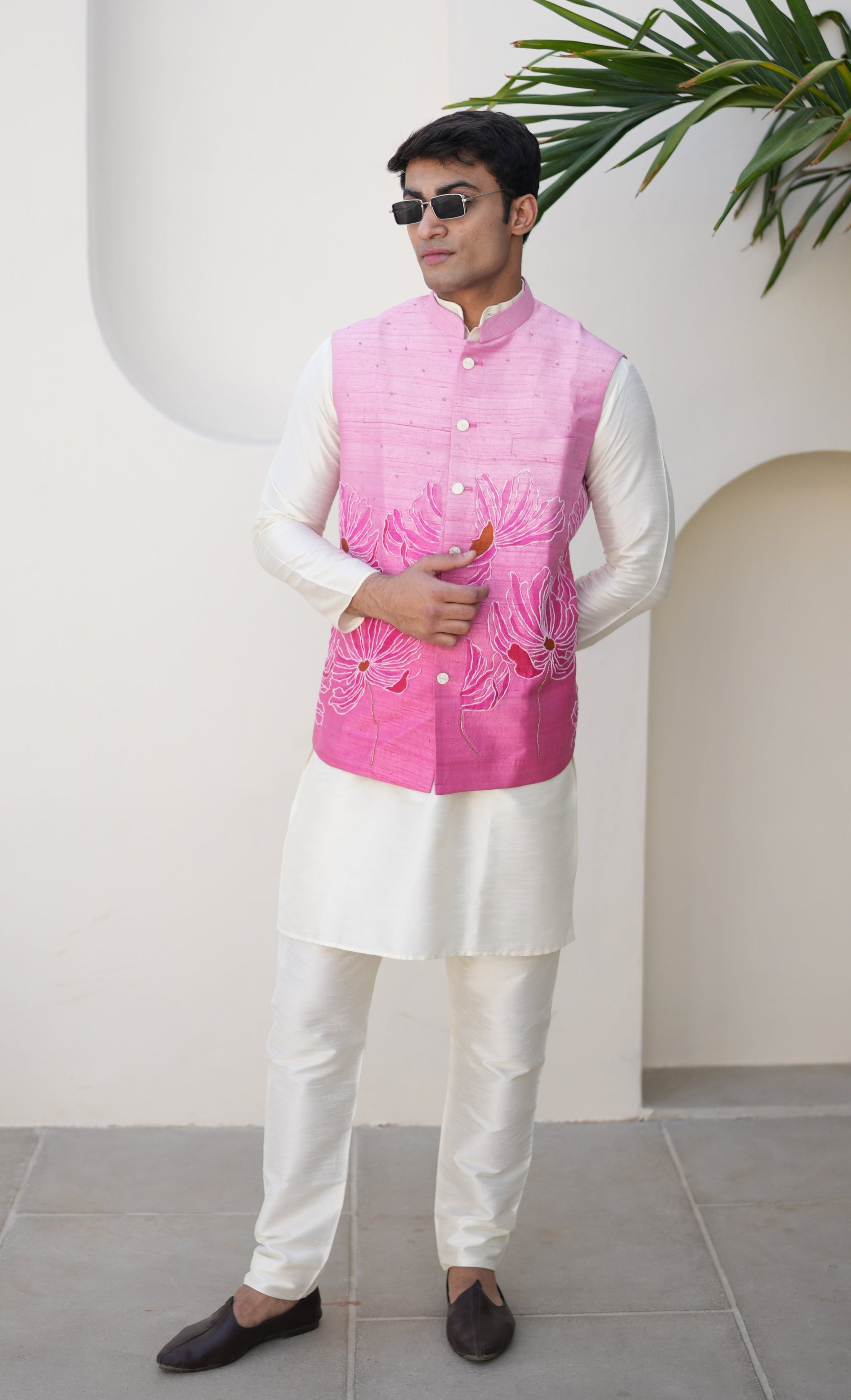 Person wearing a traditional hand painted outfit with a pink nehru jacket and white pants, standing on a light-colored floor.