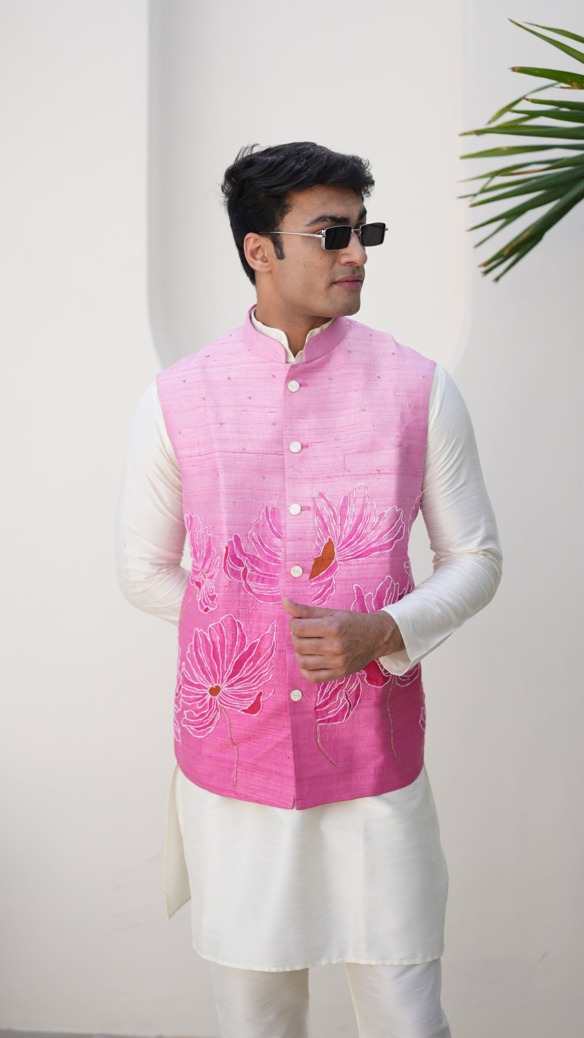 Person wearing a traditional hand painted outfit with a pink nehru jacket and white pants, standing on a light-colored floor.