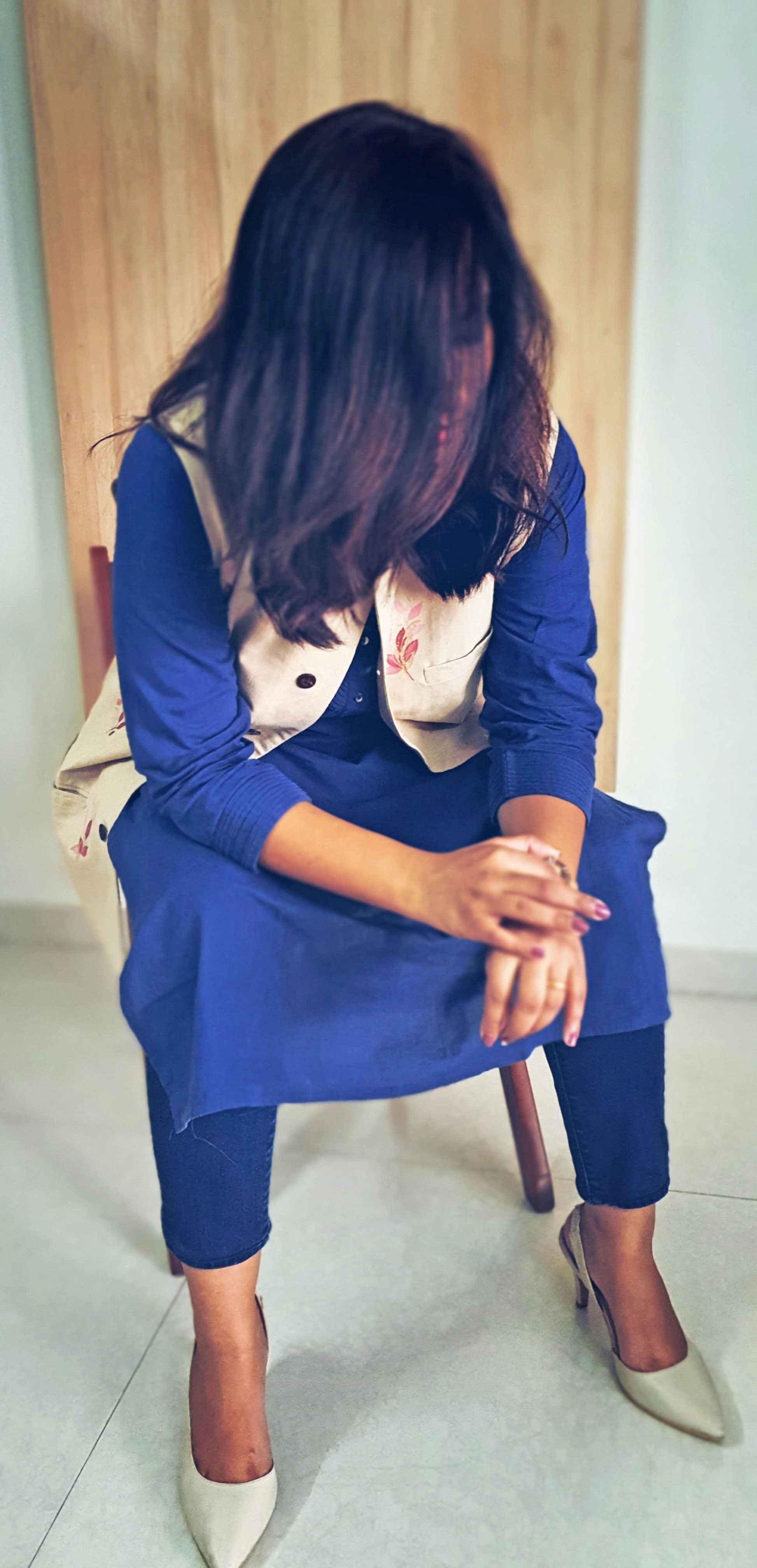 Woman in a blue outfit sitting on a chair indoors.