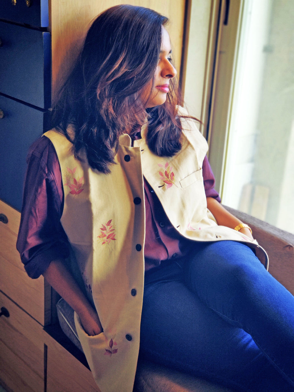 Woman wearing a cream-colored jacket with floral embroidery, sitting indoors.