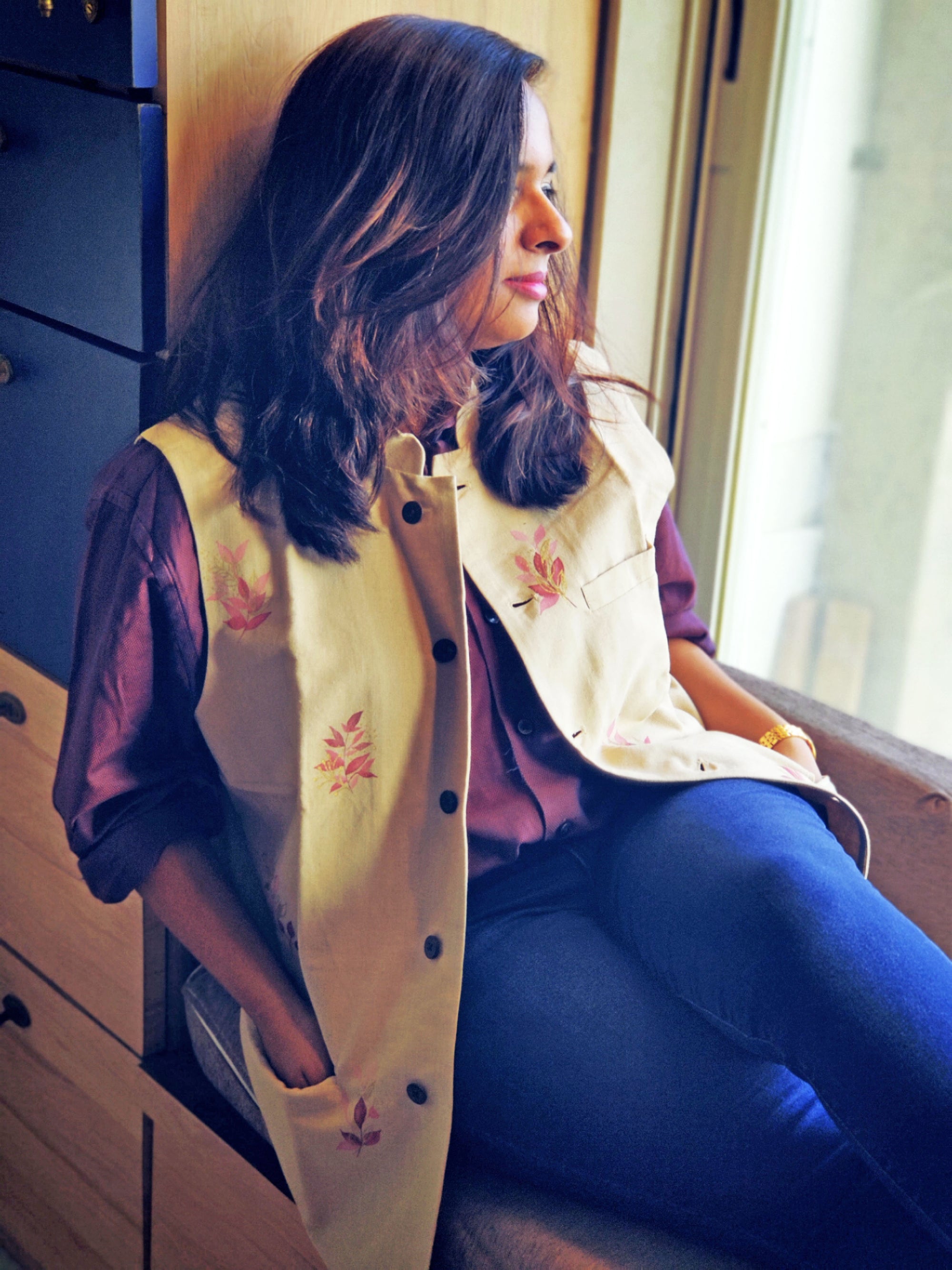 Woman wearing a cream-colored jacket with floral embroidery, sitting indoors.