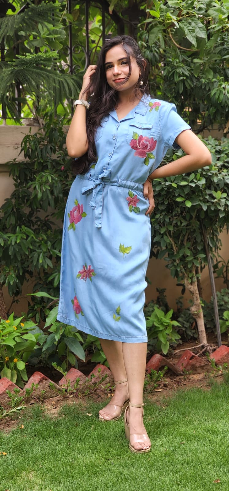 Woman wearing a light blue dress with floral patterns standing outdoors.