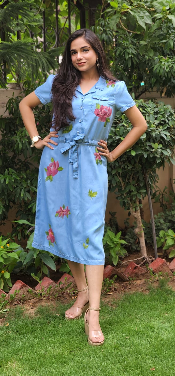 Woman wearing a light blue dress with floral patterns standing outdoors.