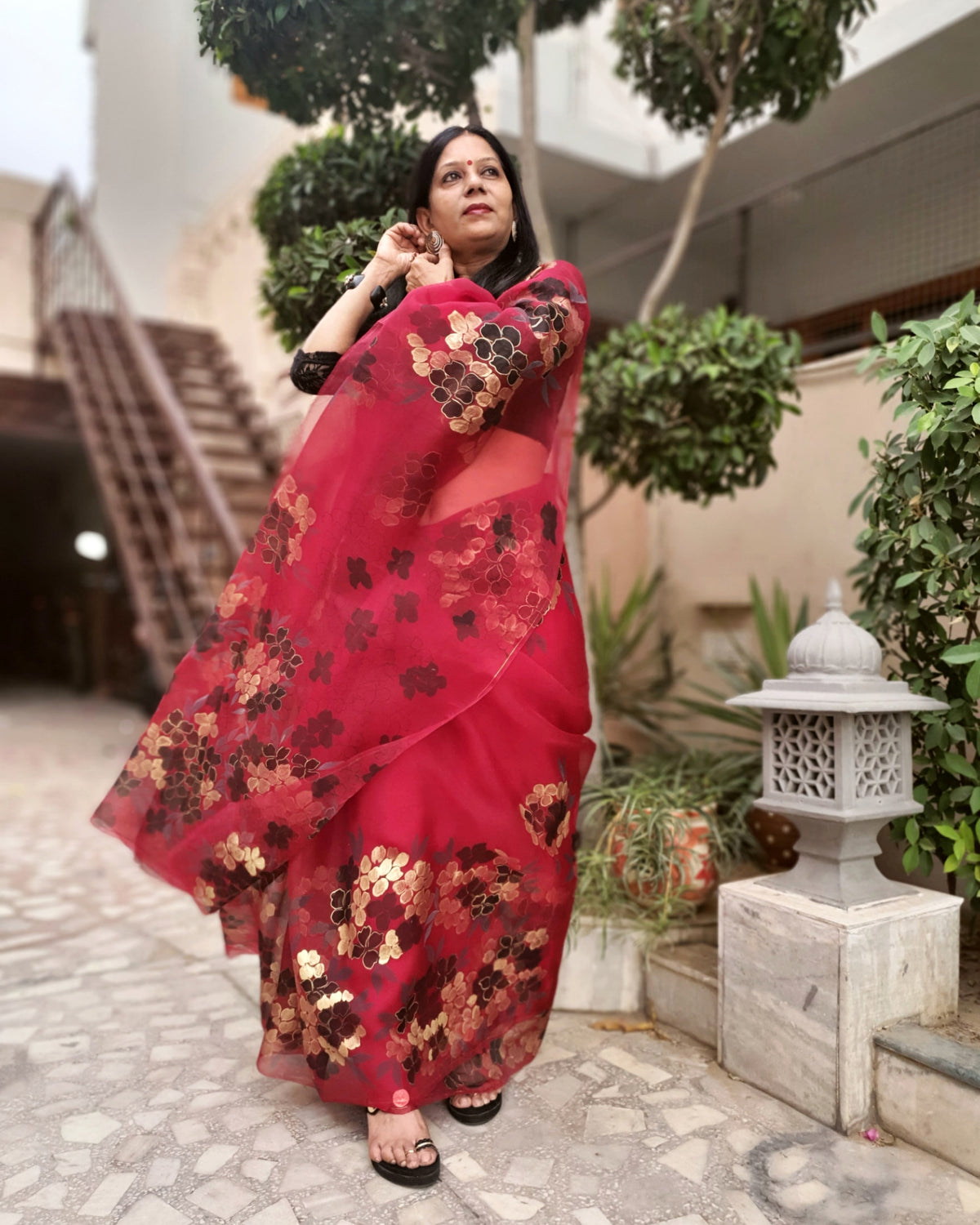 Woman wearing a red floral hand painted saree standing outdoors.