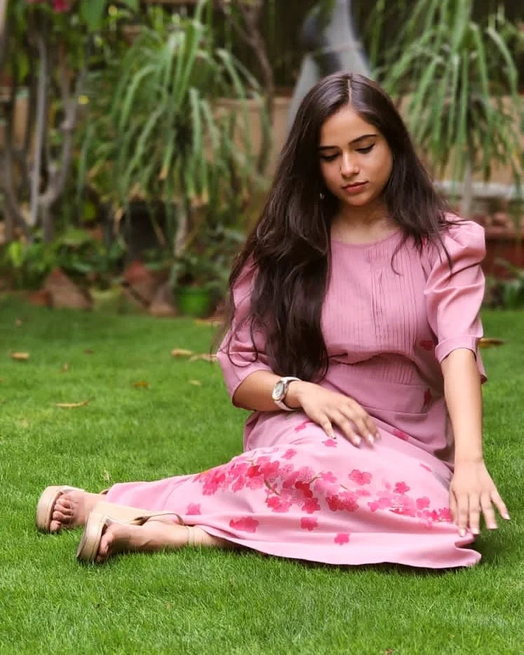 Woman in a pink dress sitting on grass with greenery in the background