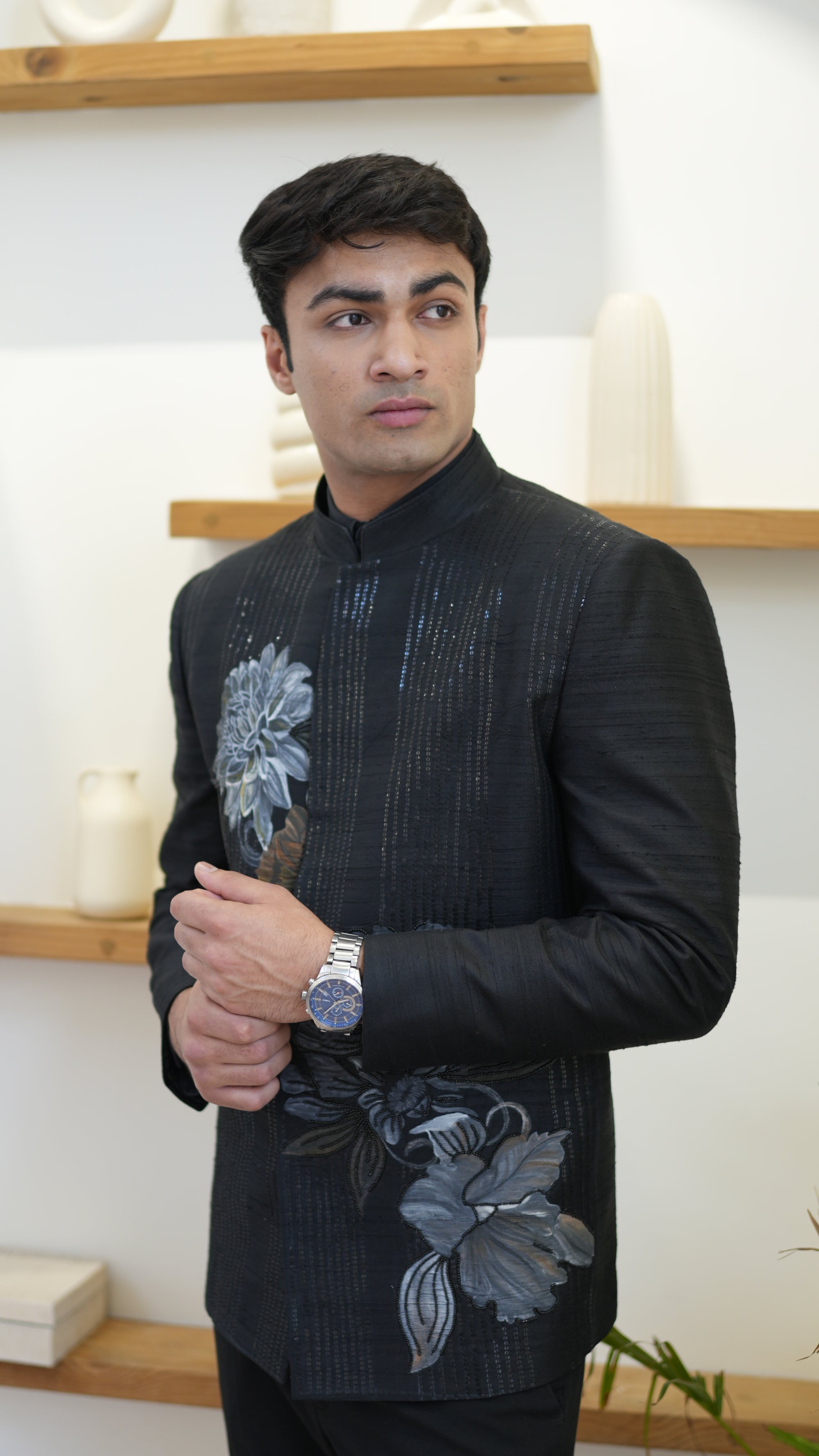 Man wearing a black hand painted Bandhgala with floral designs indoors.