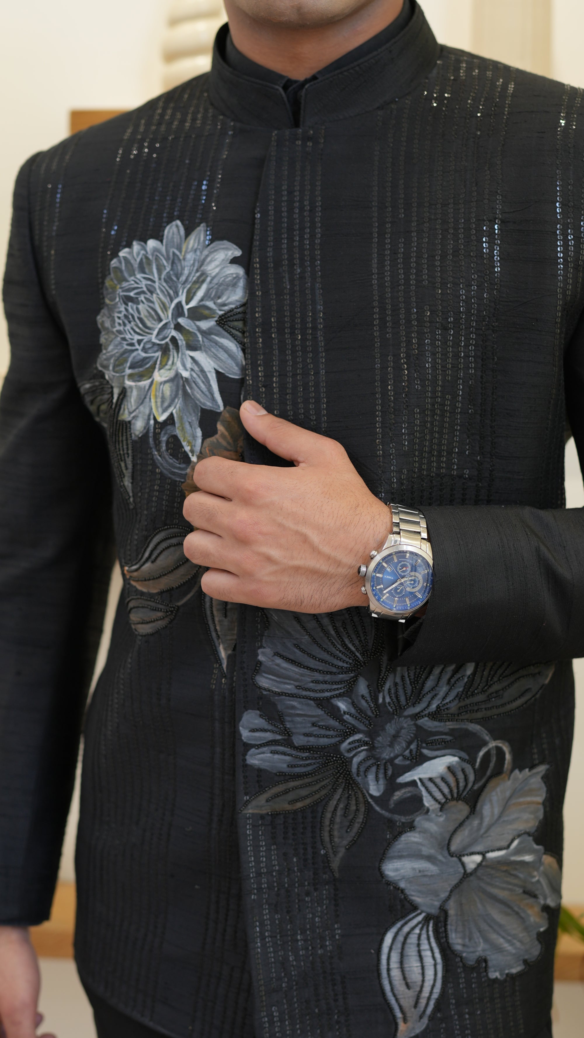 Man wearing a black hand painted Bandhgala with floral designs indoors.