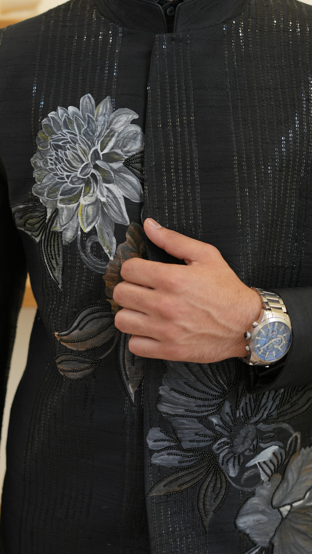 Man wearing a black hand painted Bandhgala with floral designs indoors.