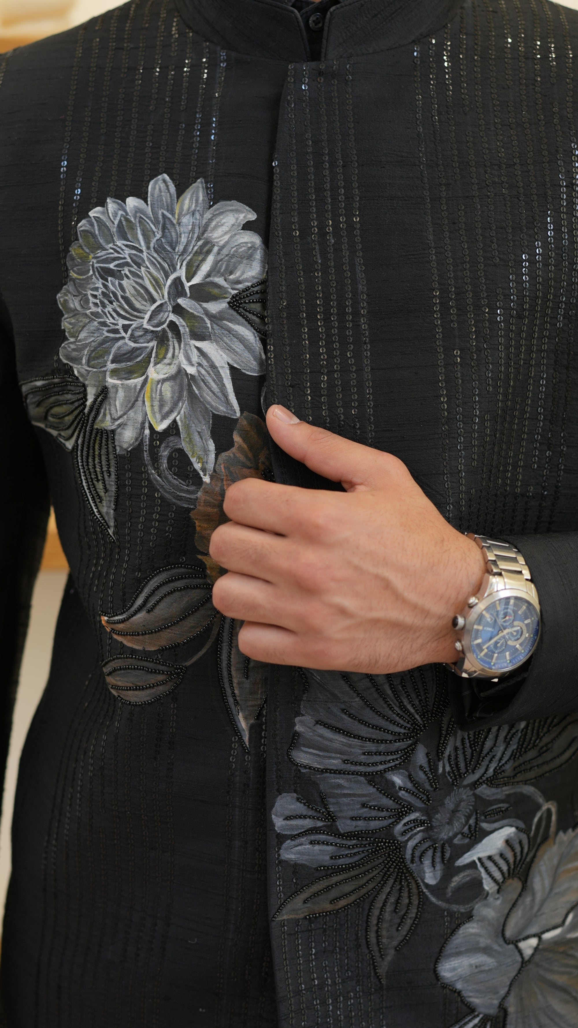 Man wearing a black hand painted Bandhgala with floral designs indoors.