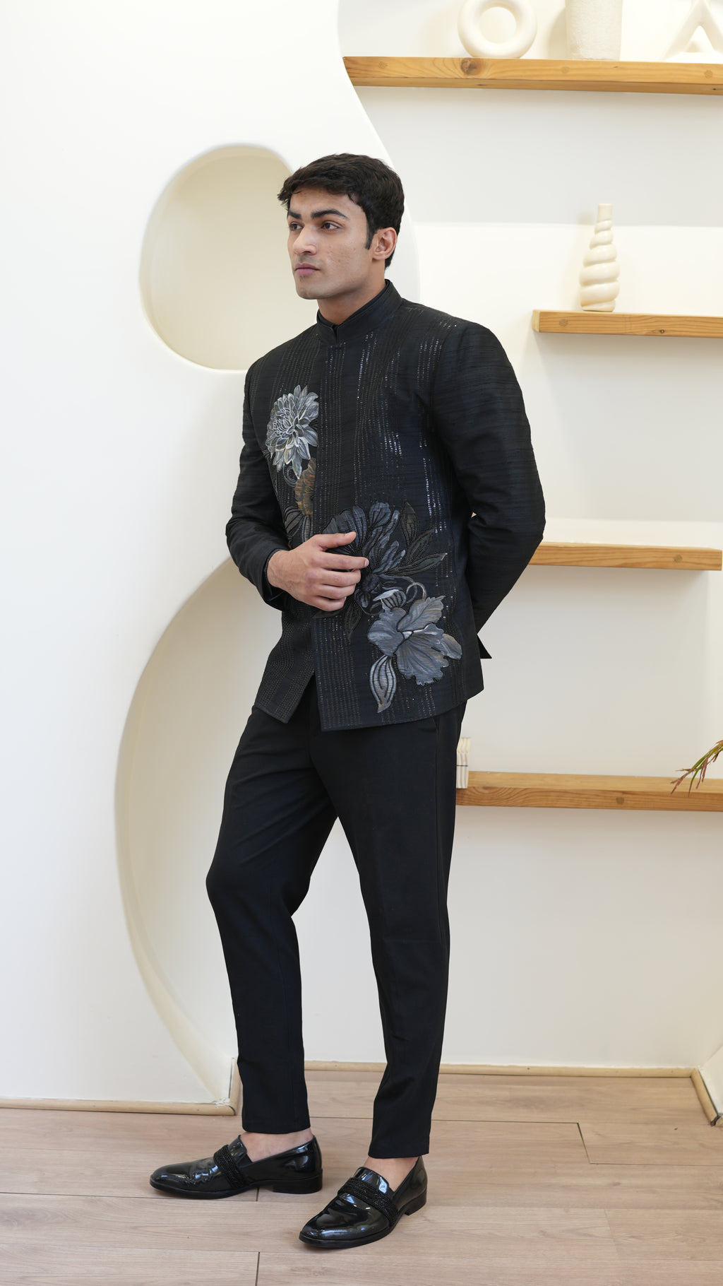 Man wearing a black hand painted Bandhgala with floral designs indoors.