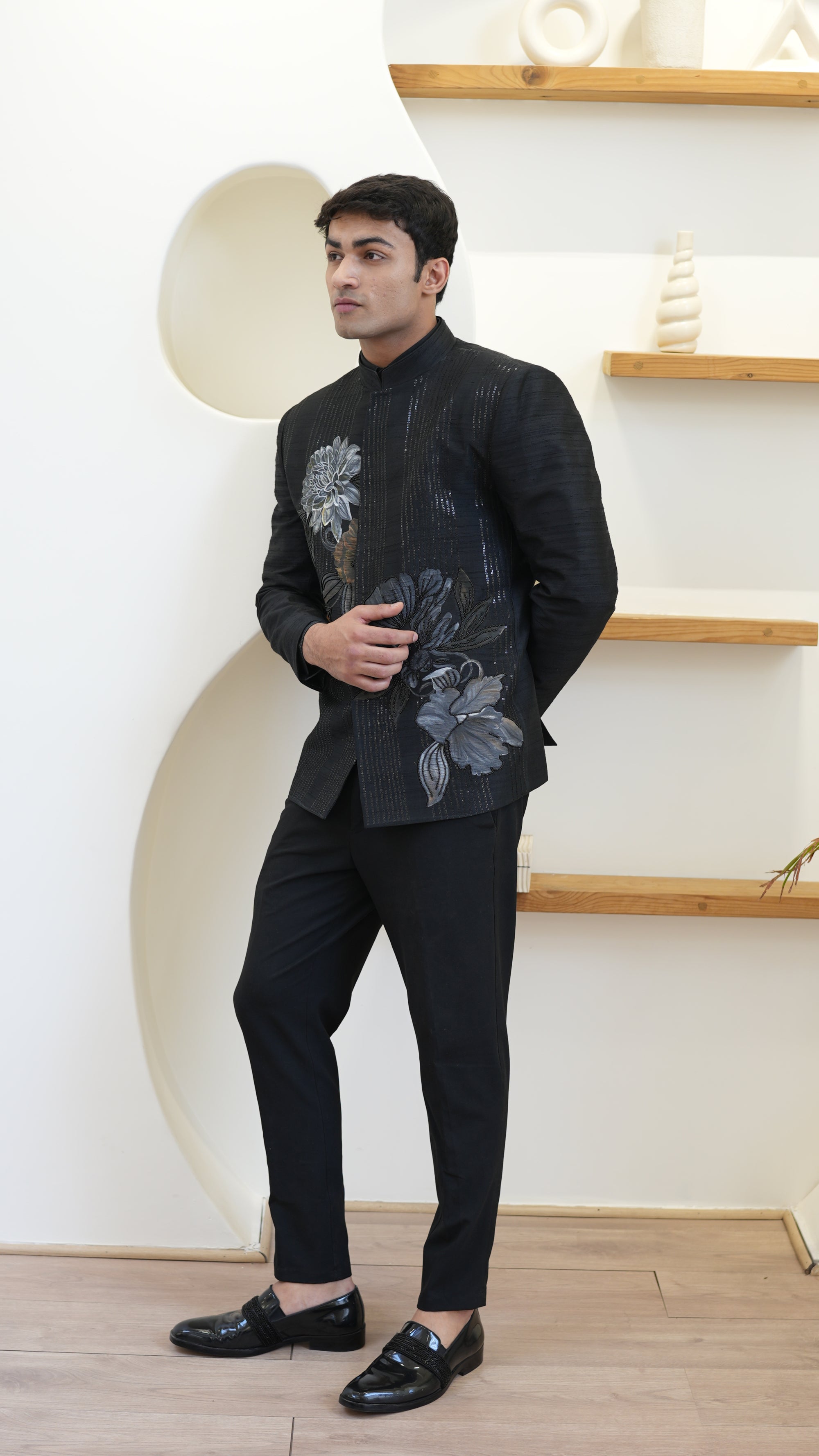 Man wearing a black hand painted Bandhgala with floral designs indoors.