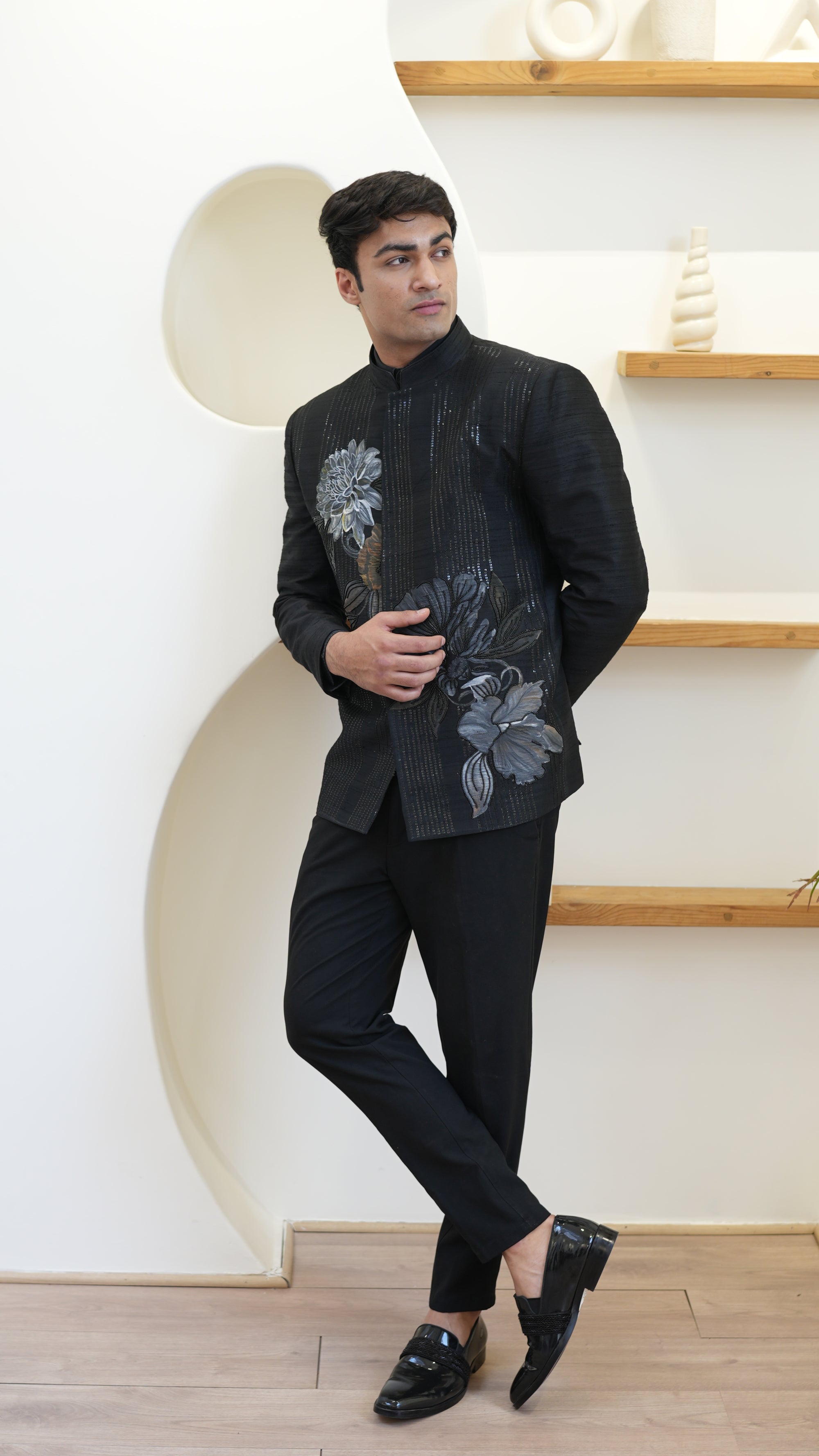Man wearing a black hand painted Bandhgala with floral designs indoors.