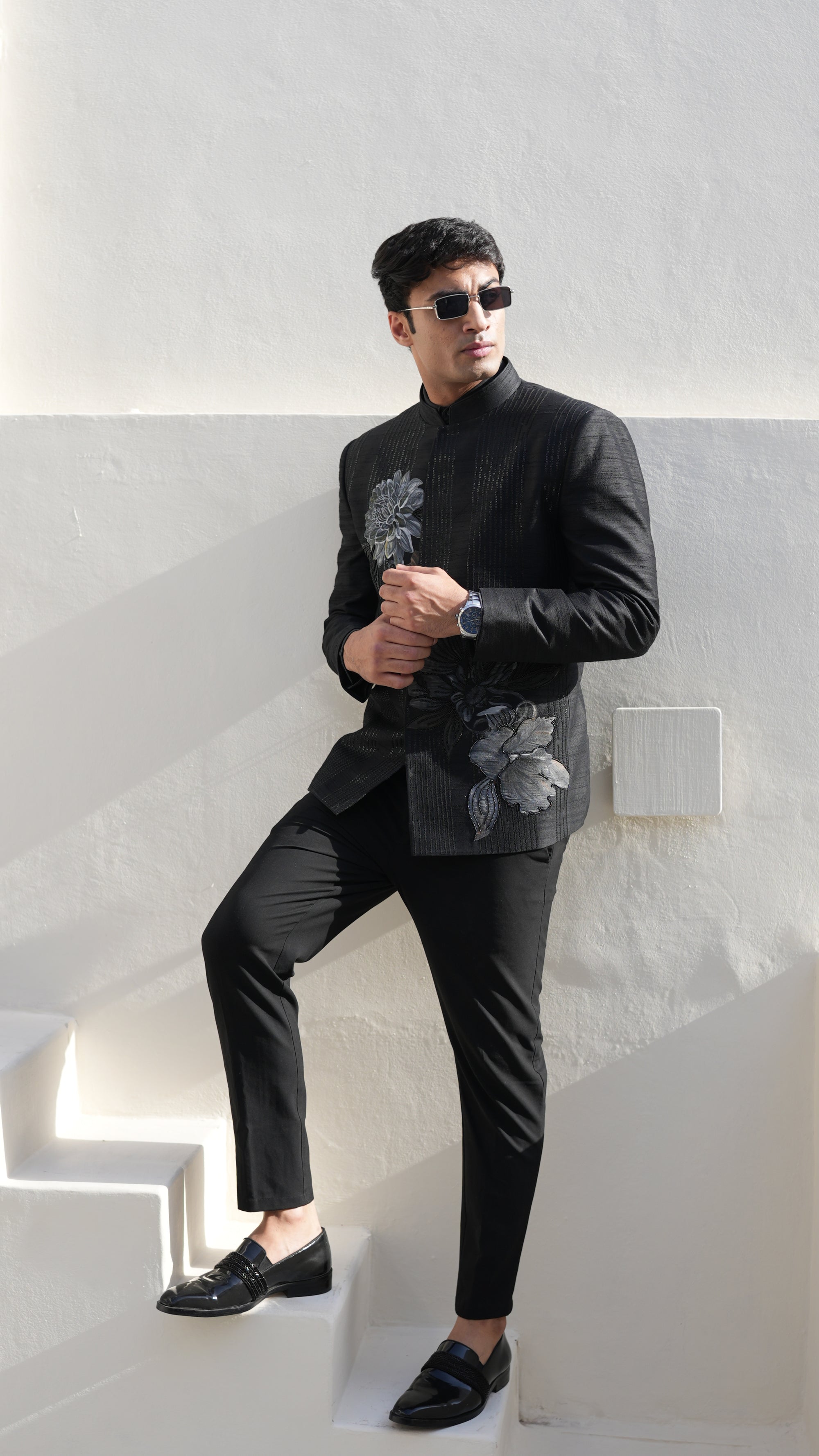 Man wearing a black hand painted Bandhgala with floral designs indoors.