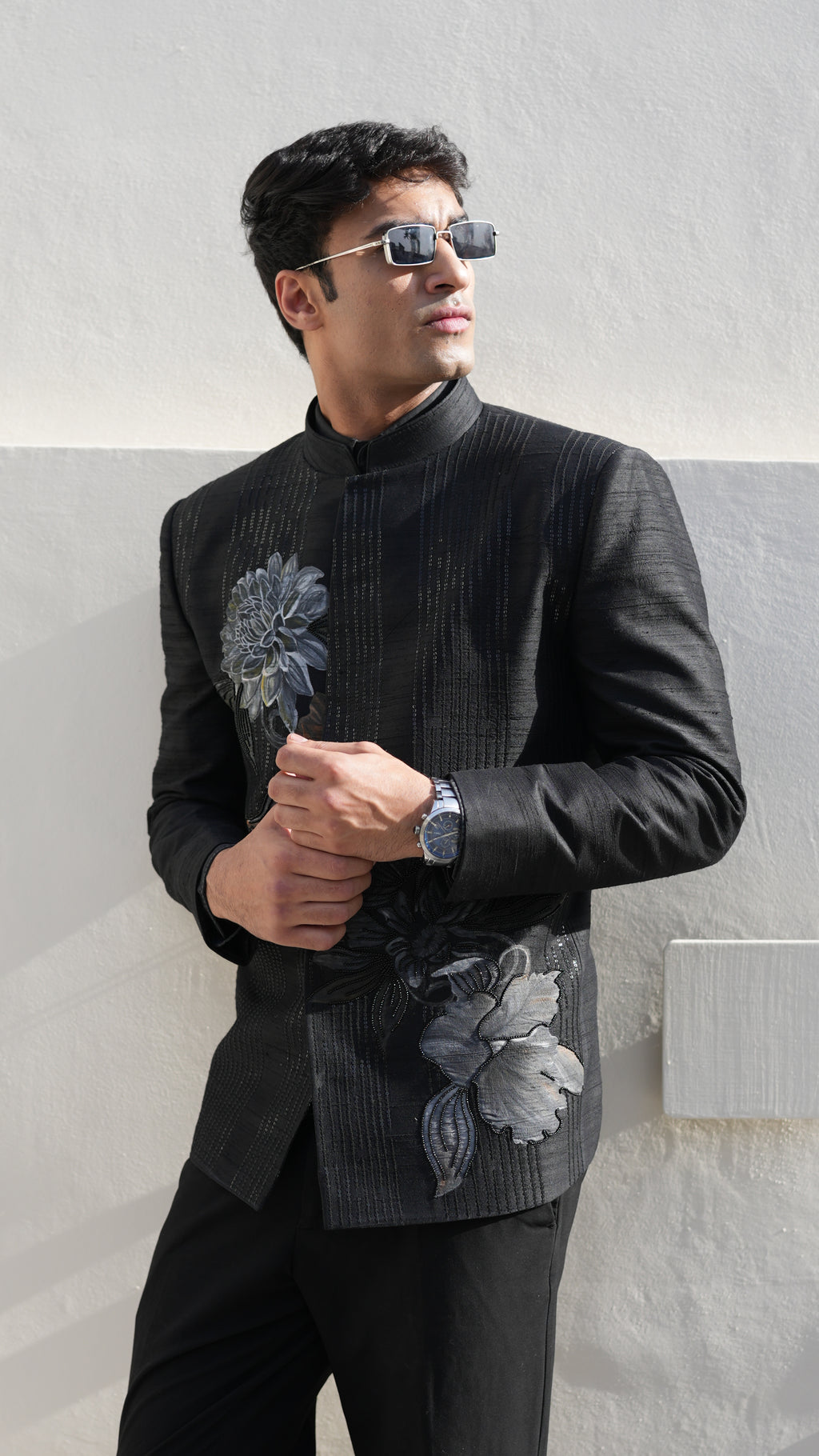 Man wearing a black hand painted Bandhgala with floral designs indoors.