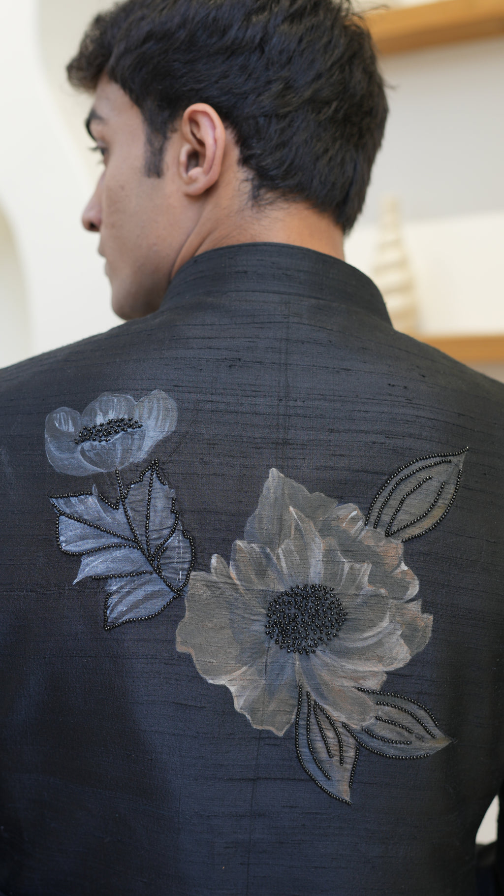 Man wearing a black hand painted Bandhgala with floral designs indoors.