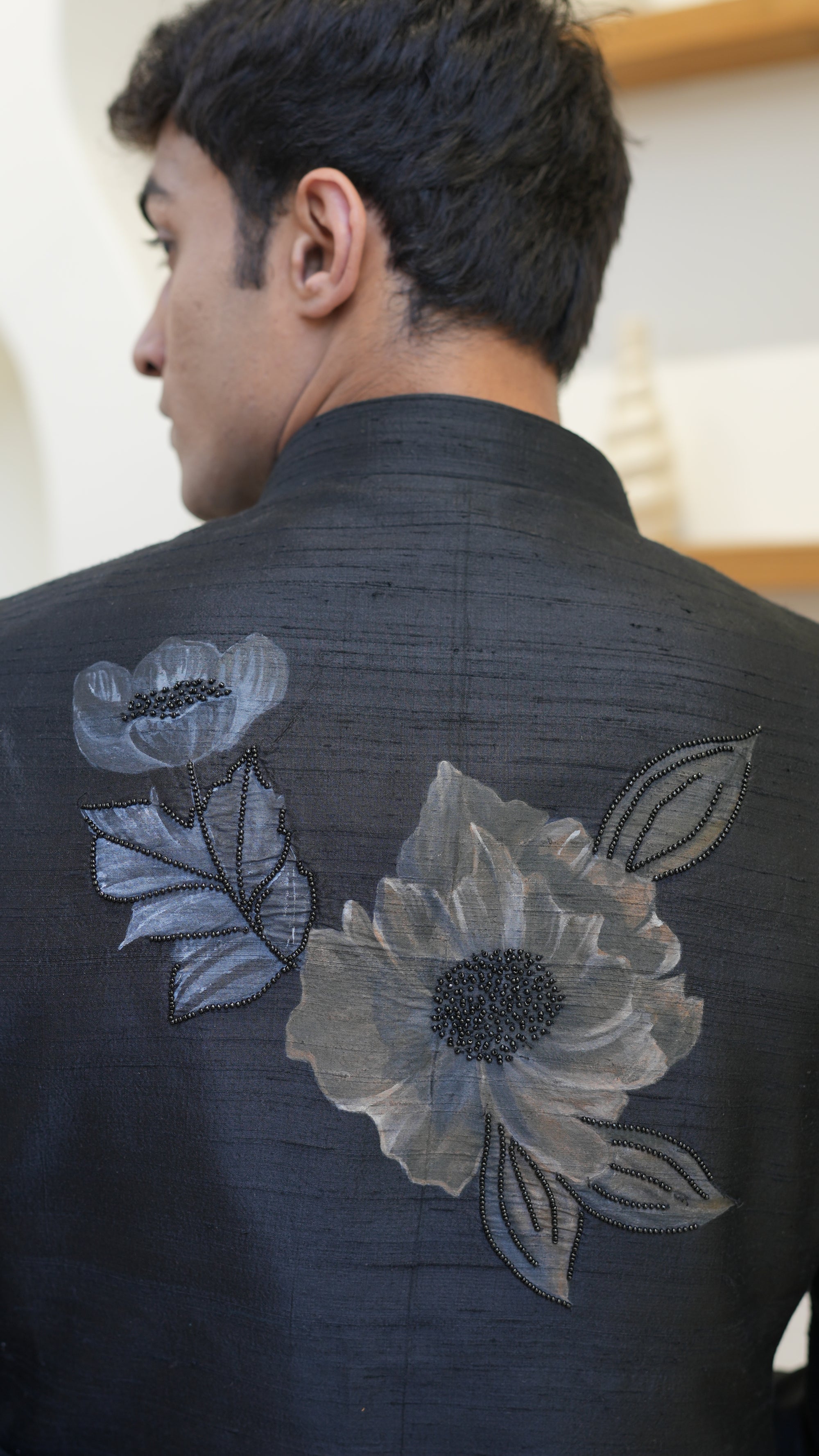 Man wearing a black hand painted Bandhgala with floral designs indoors.