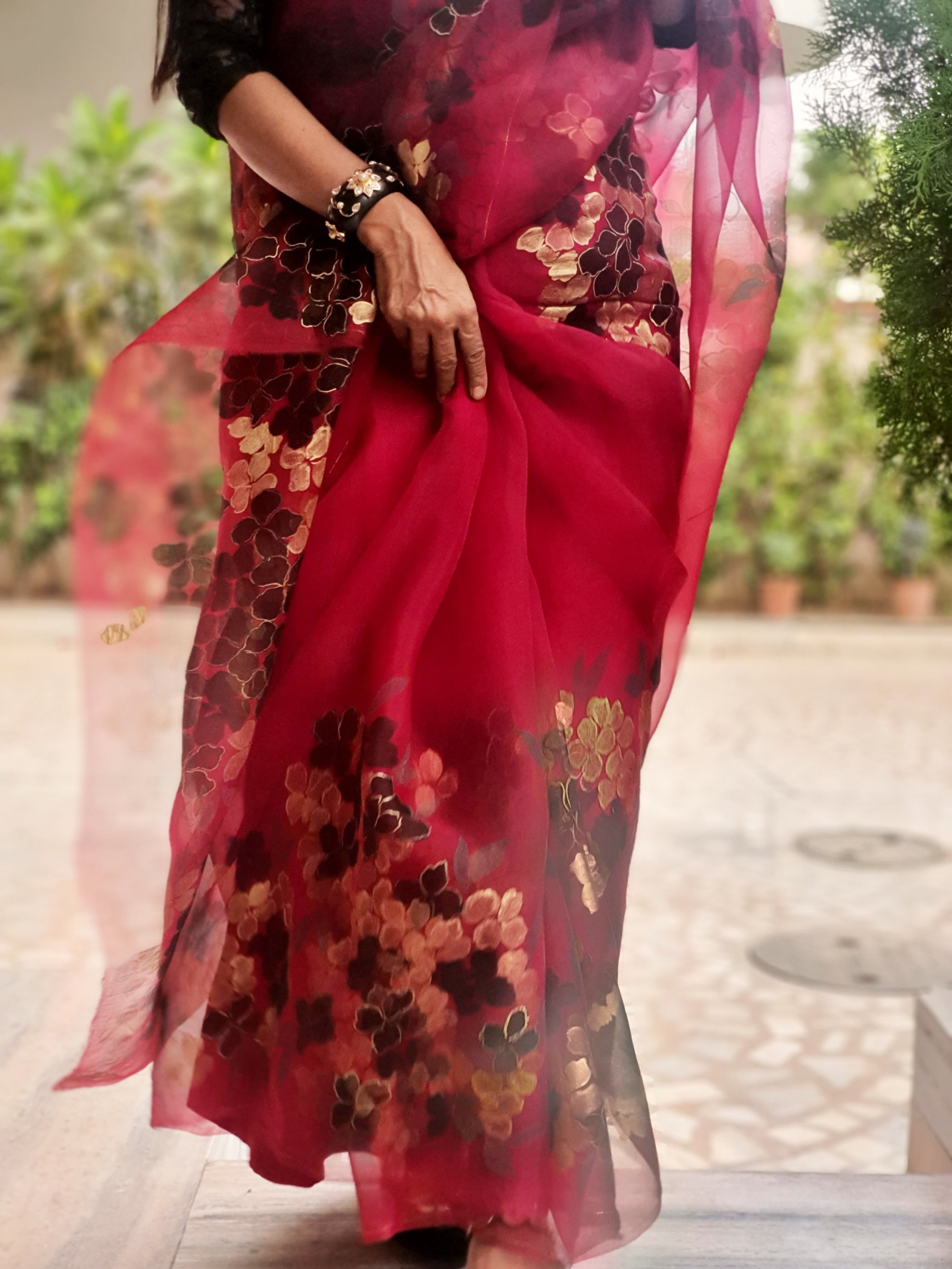 Red saree with floral patterns held by a person outdoors