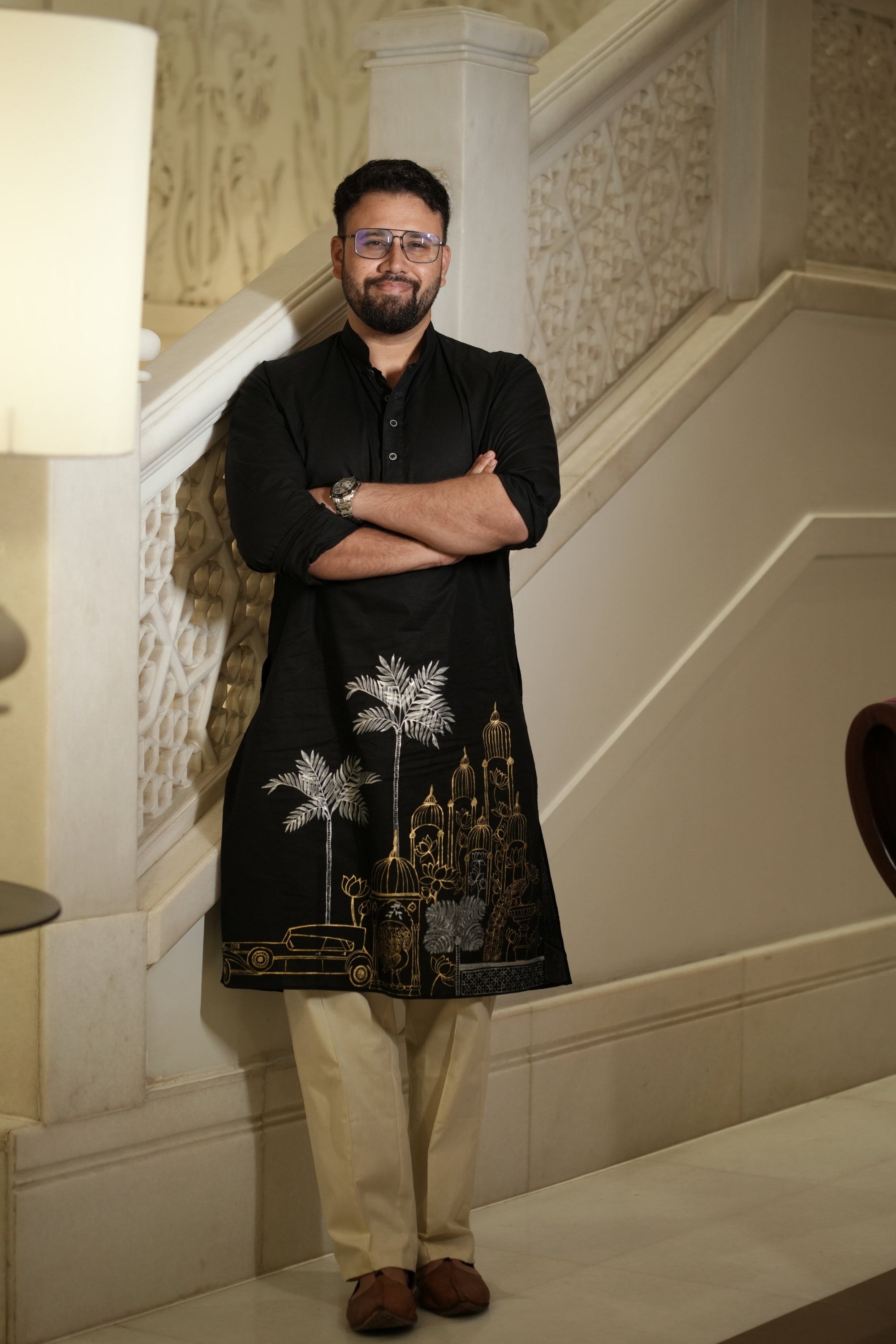 Man wearing a black hand painted kurta with beige pants.