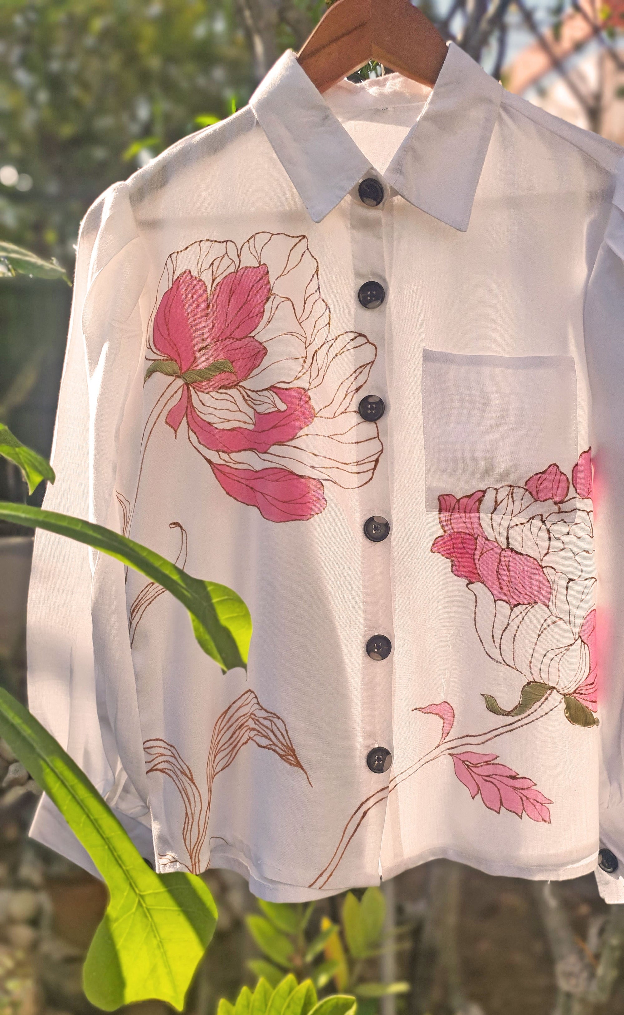 White shirt with pink floral patterns hanging against a natural background