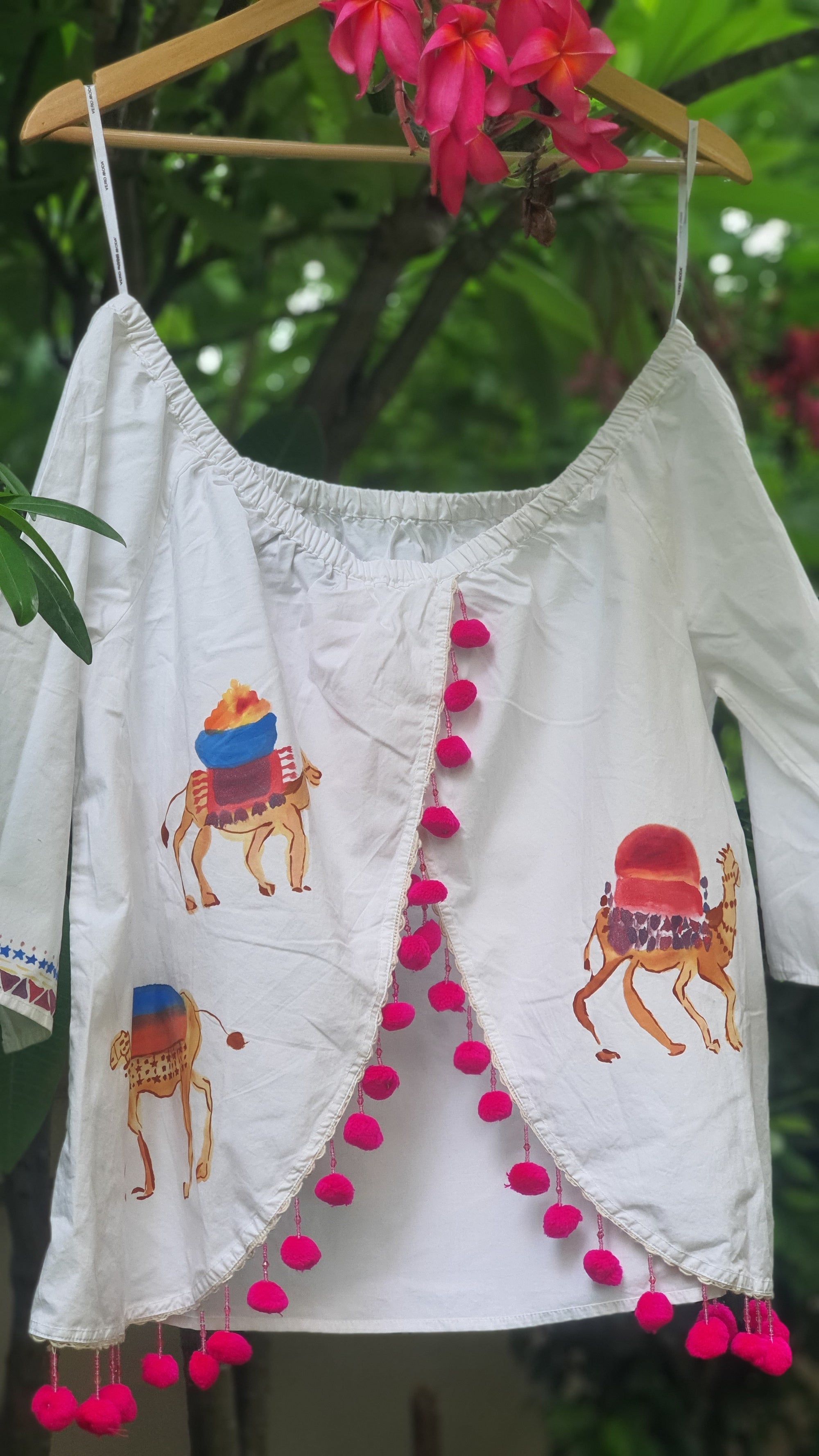 White embroidered garment with pink pom-poms on a green background