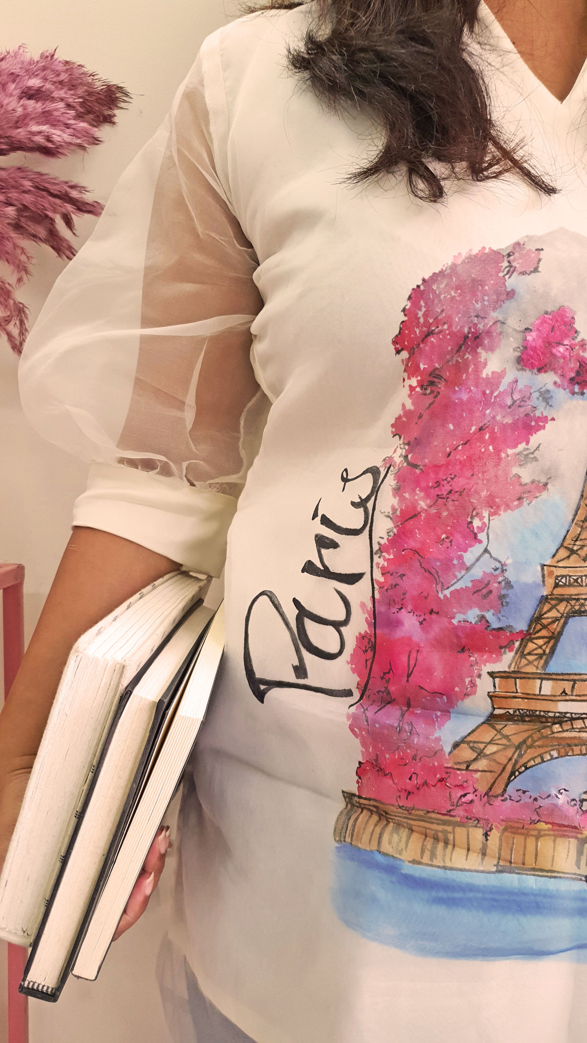 Person wearing a white shirt with a colorful 'Paris' design holding a book.