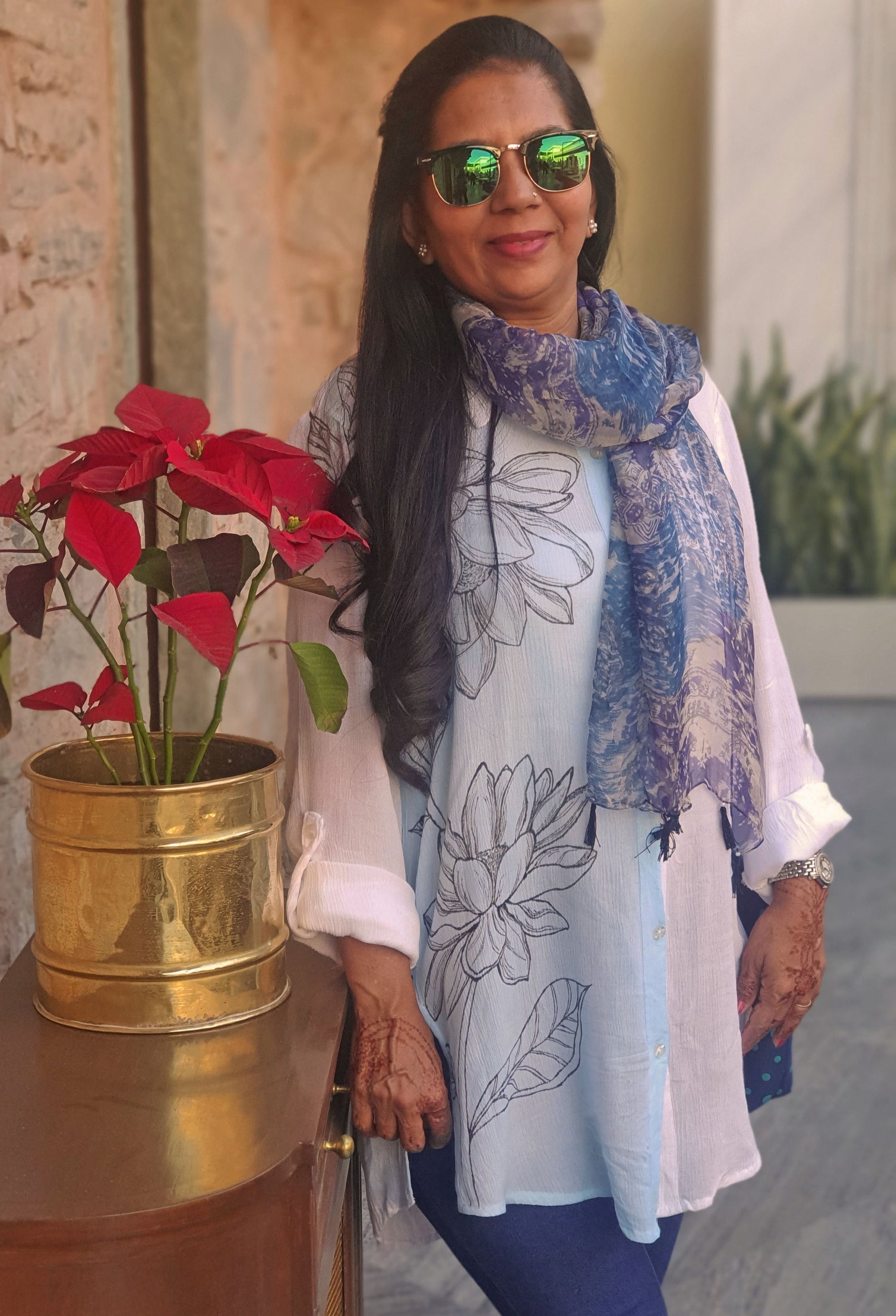Woman wearing hand painted white shirt standing next to a potted plant.